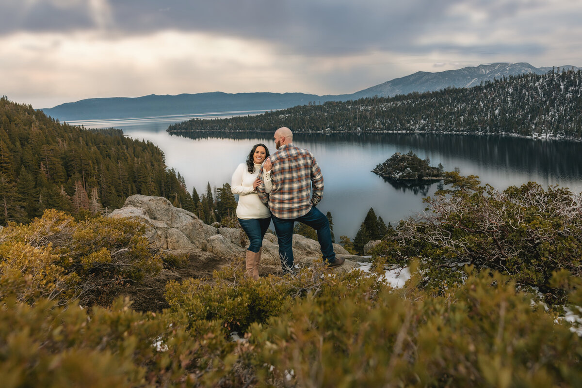 Woman and man stand in front of Emerald Bay in Lake tahoe and hold each other.