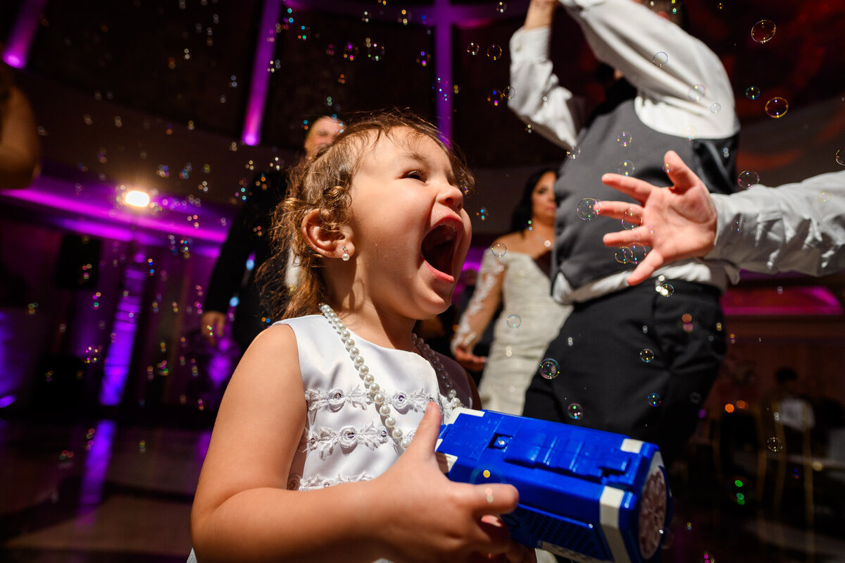 A young girl laughs with joy surrounded by bubbles on the wedding dance floor