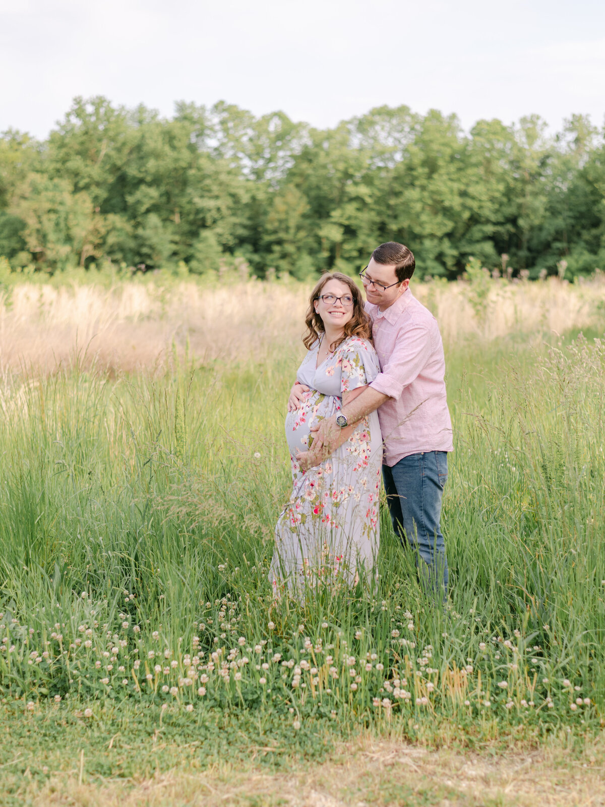 Expecting parents staring at each other while standing in tall grass.