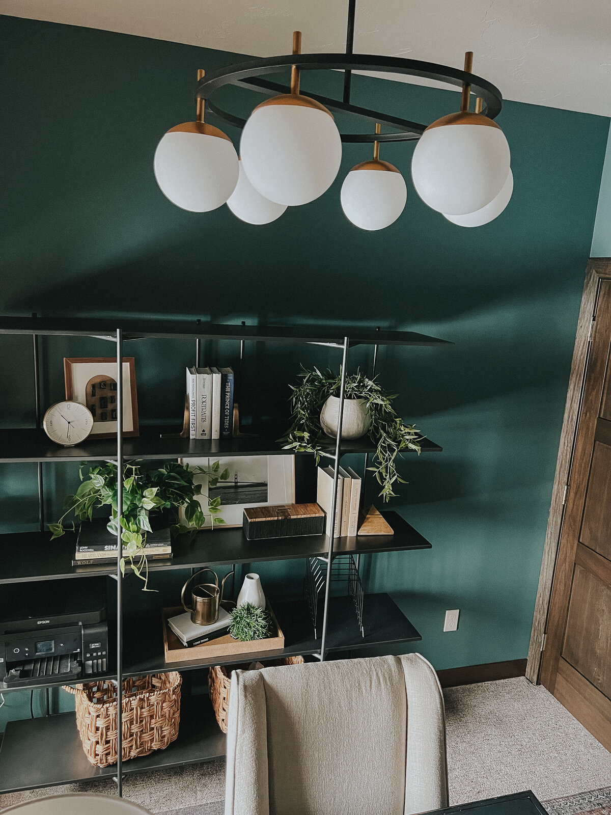 A hanging chandelier with white frosted glass globes hangs over a desk