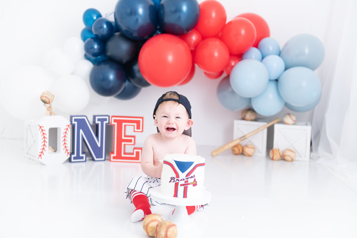 A young toddler smashes a baseball themed cake in a childrens photographer Atlanta studio