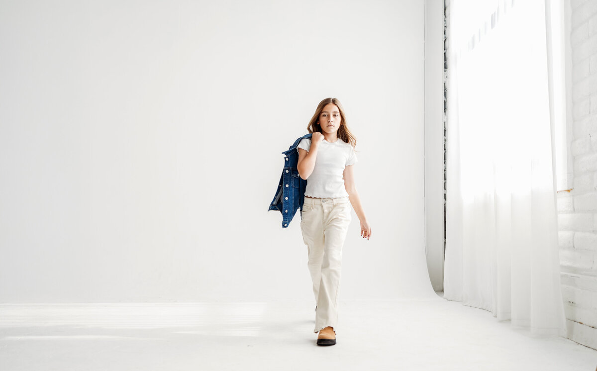 Tween girl walks towards camera on all white background in photo studio