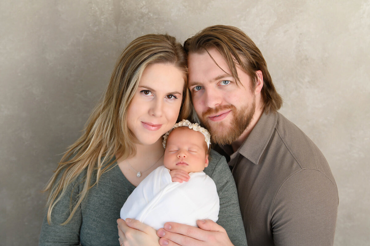 mom and dad holding their newborn girl wrapped in white for their Burlington, On newborn photos