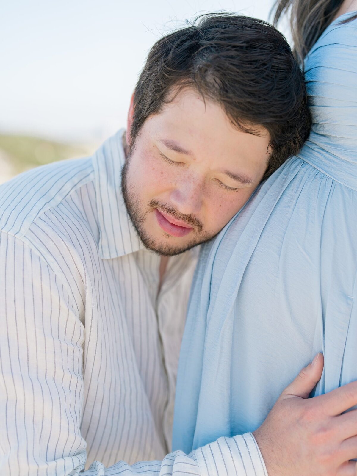 Father listening to babys heartbeat in moms belly during maternity session at San Diego beach