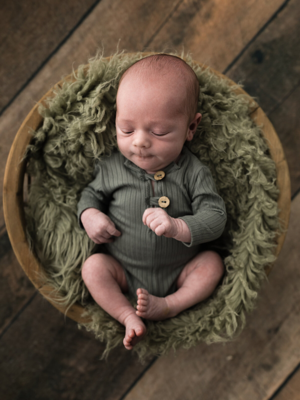 newborn baby boy in green onesie laying in basket for studio portraits in cleveland ohio