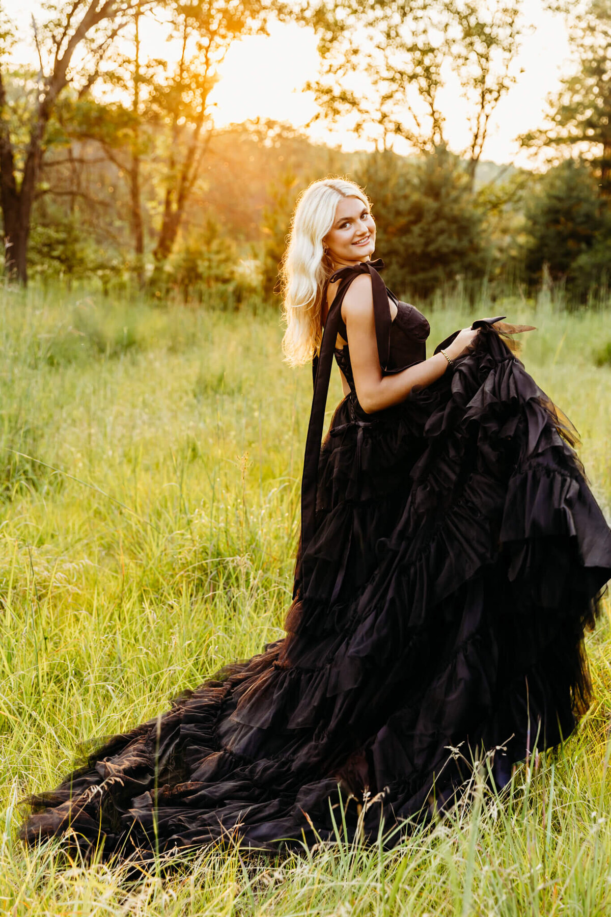 gorgeous oshkosh high school senior playing with the skirt on her large black gown as she smiles while walking in a field