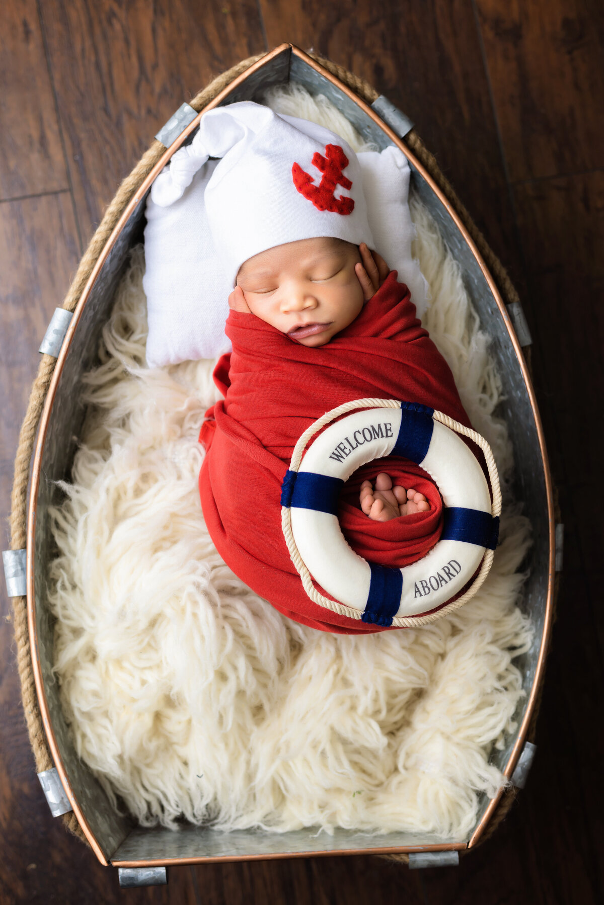 Newborn Photographer, a  baby sleeps in a boat shaped basket on a fluffy blanket, there a lifesaver that reads "welcome aboard"