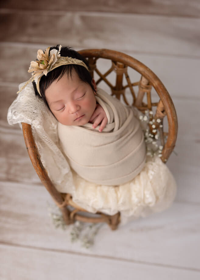 This boho style photo was taken on a white barnwood floor.  The baby is in a rattan high backed chair draped with lace and accented with babies breath and a cream wrap and headband