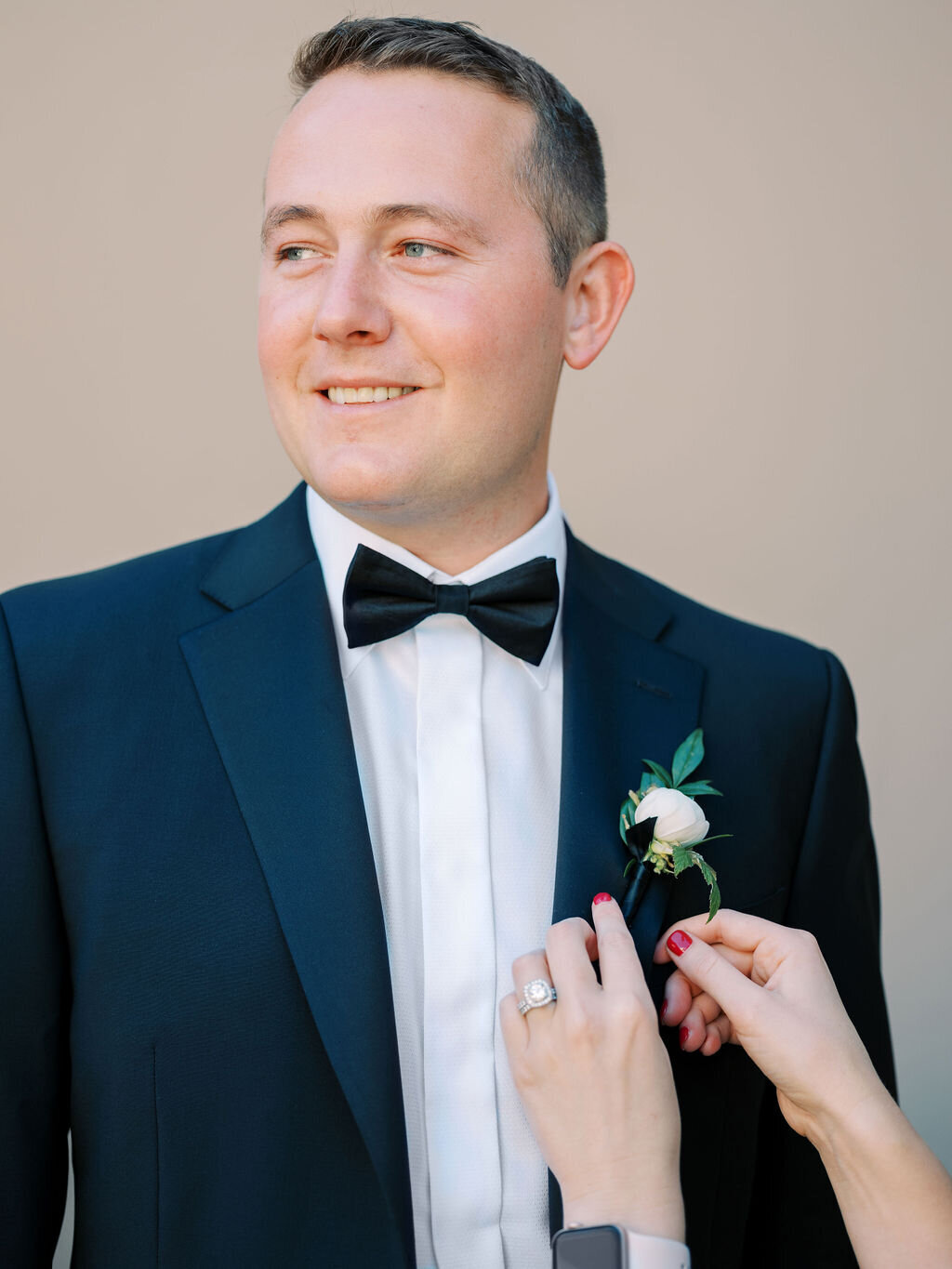 A close-up of a groom getting his boutonniere pinned on his classic black tuxedo. The perfect detail for a refined wedding look.