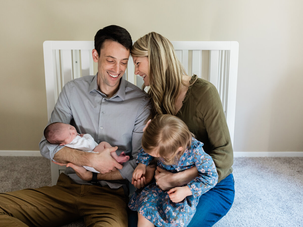 parents laughing holding newborn baby boy and toddler for in home lifestyle photography session