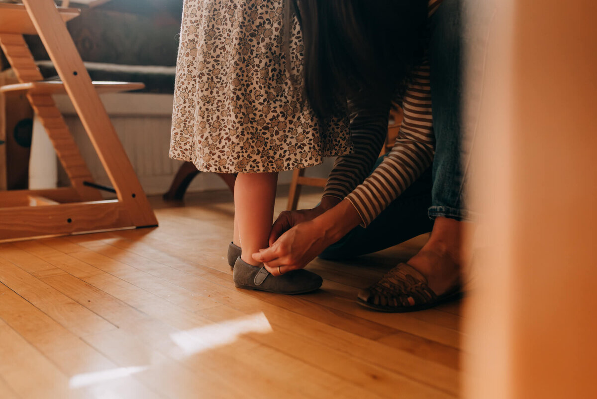 A mother helps her daughter put on her shoes before going outside