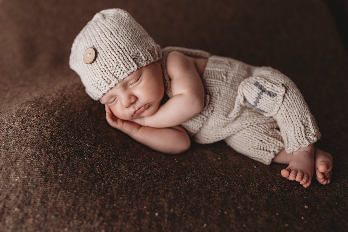 A baby laying on a brown blanket in a knit sweater.