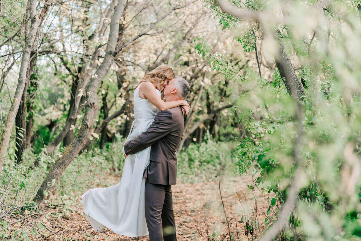 Bride and groom share a kiss while he lifts her up.
