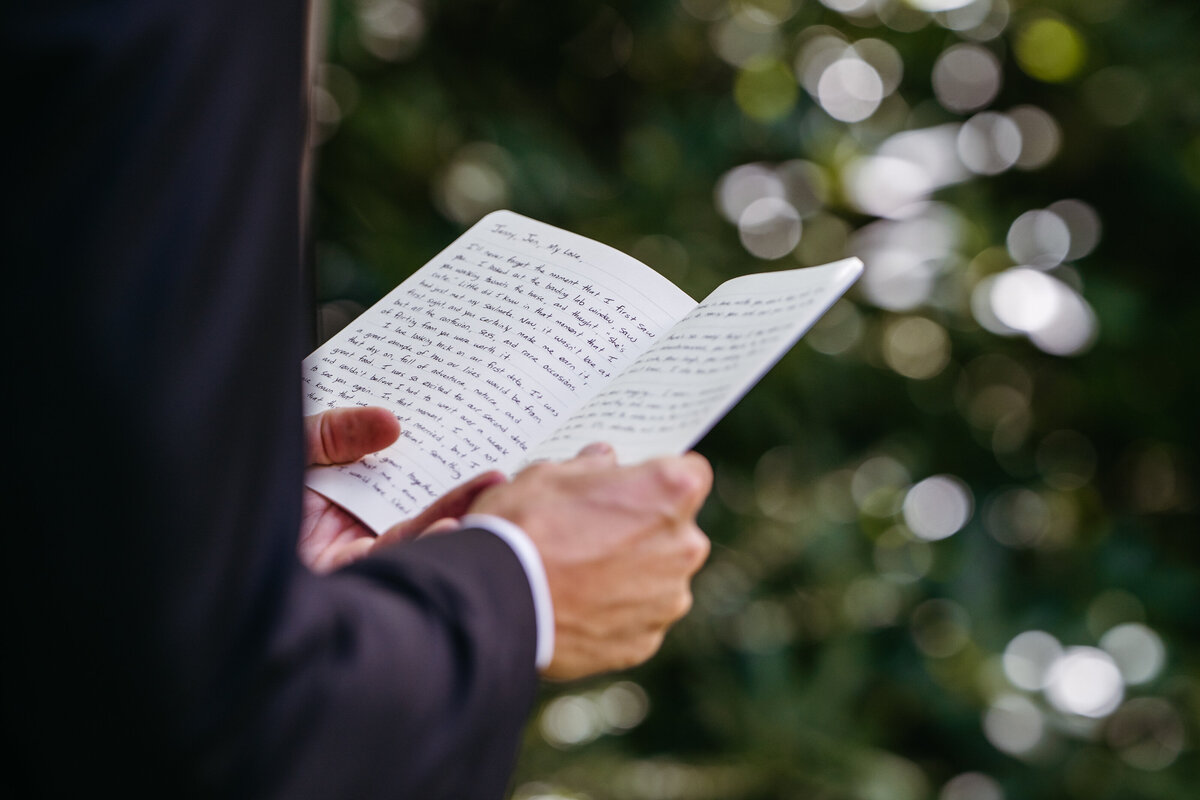 Groom reading vows in shaded garden area