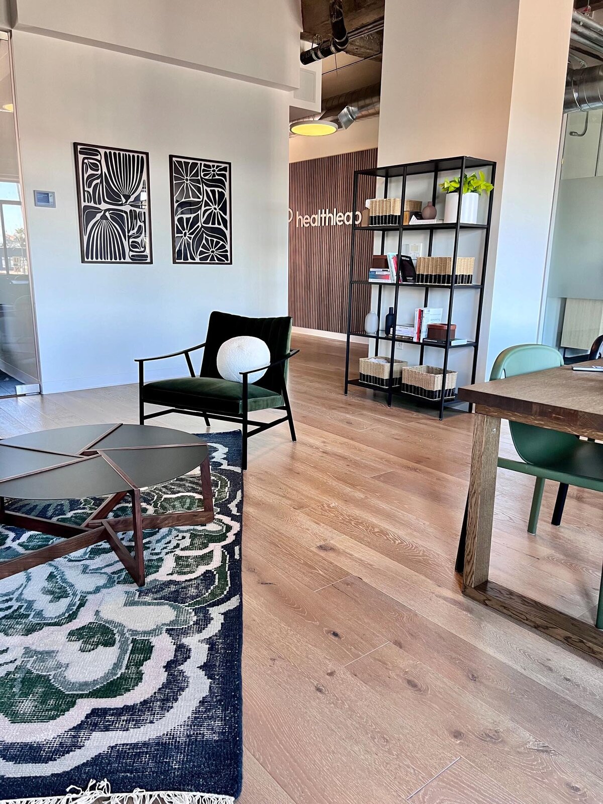 Lounge area with a green velvet chair, black metal shelving unit, abstract black-and-white artwork, and a patterned rug with green accents.