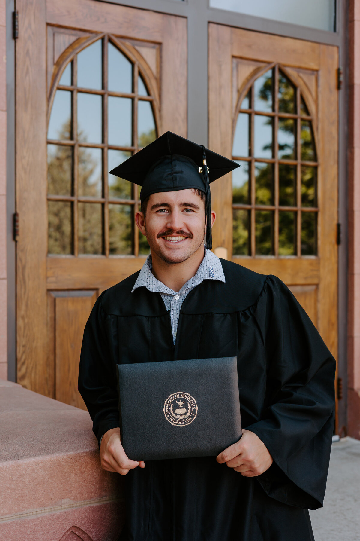 A young man in graduation attire holding up a diploma