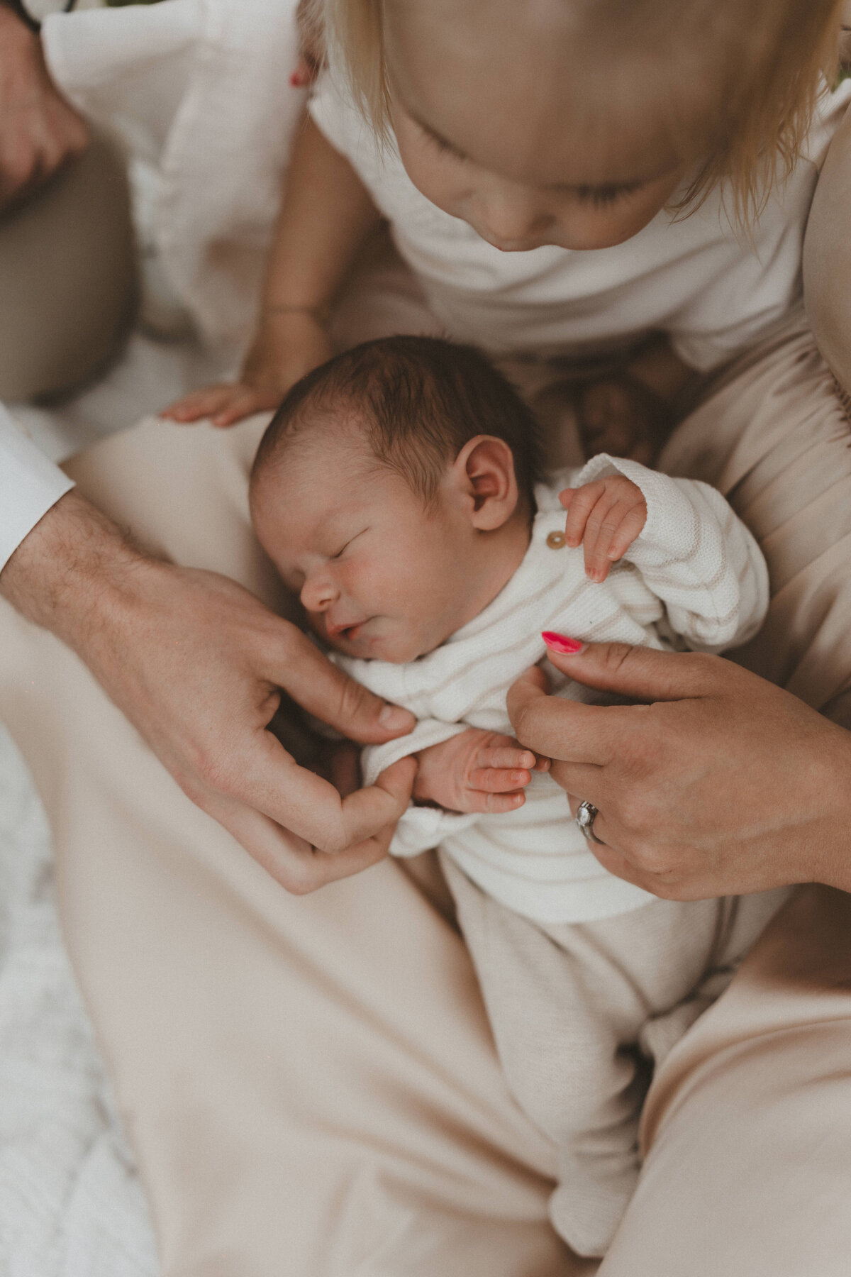 Foto van newborn baby met handen van mama en papa en zusje.