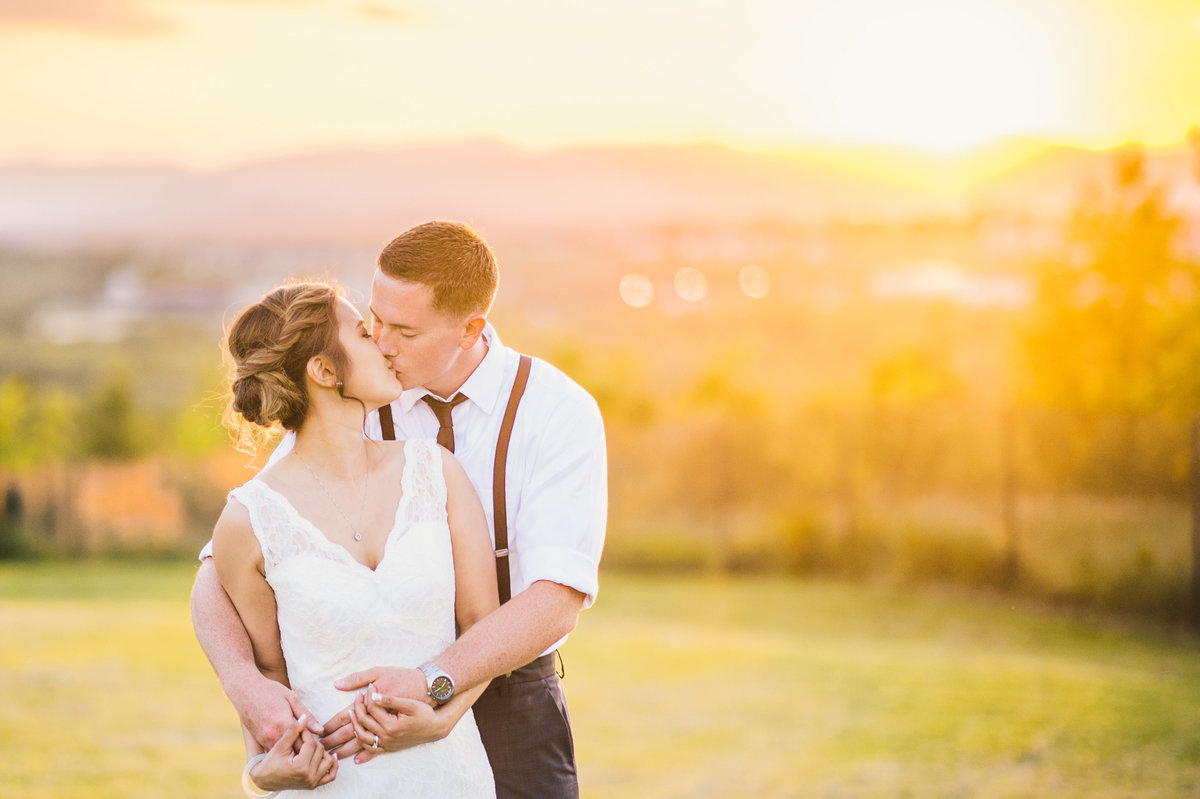 Bride and groom kissing with a glowing sun setting behind them.