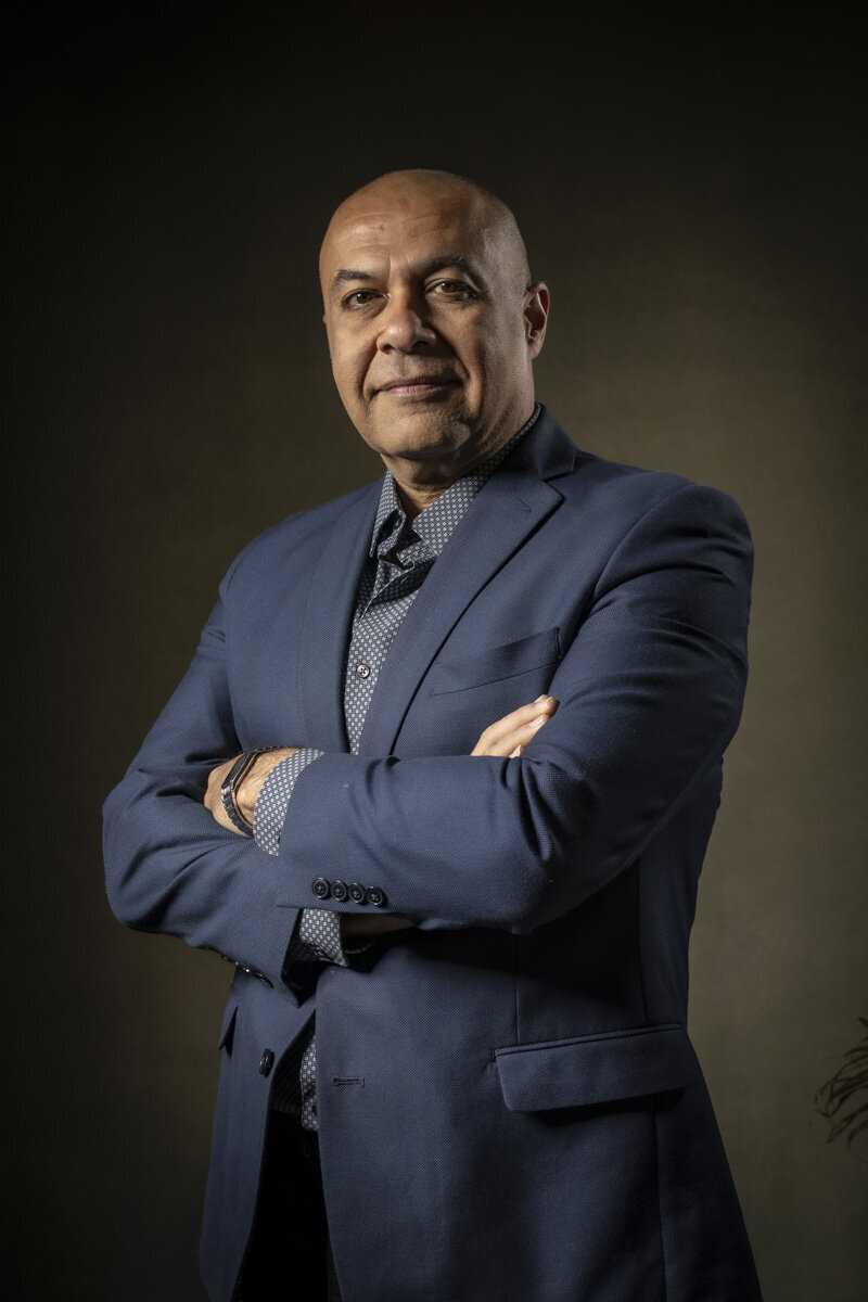 Headshot in MA of smiling man in blue jacket, arms crossed, against warm gray background by Rob Faber Photography.