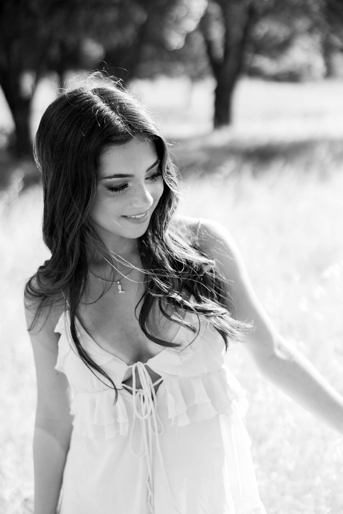 Black and white photo of a brunette girl wearing a white dress and looking down at the ground