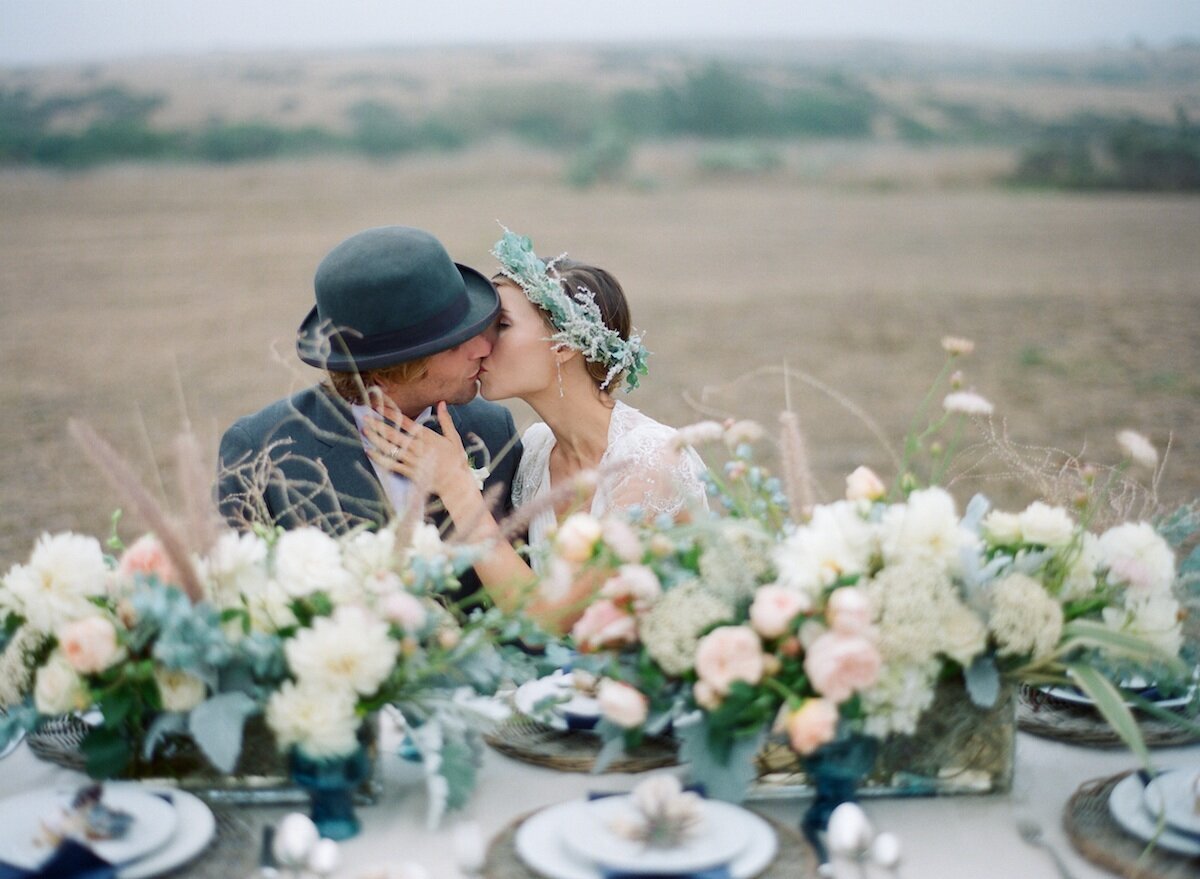 bride and groom sitting at a long head table with flowers