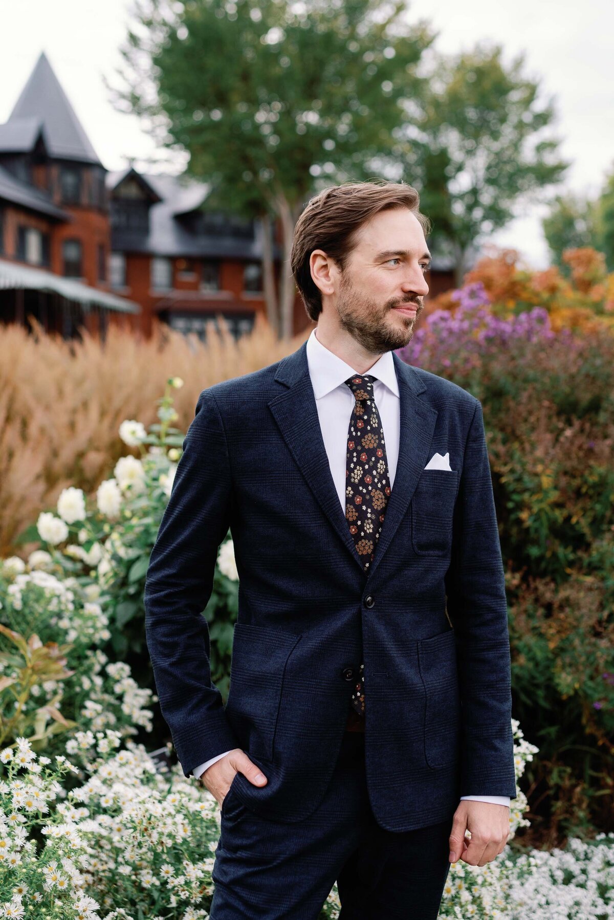groom looks away from camera at shelburne farms surrounded by florals