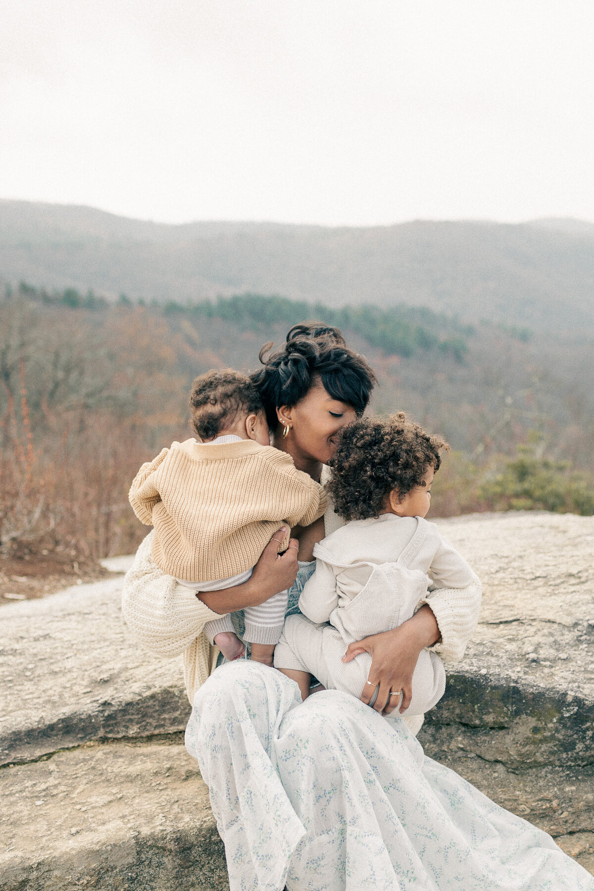 Family picture of mother and toddler sons as she snuggles them on top of a Kansas City look out