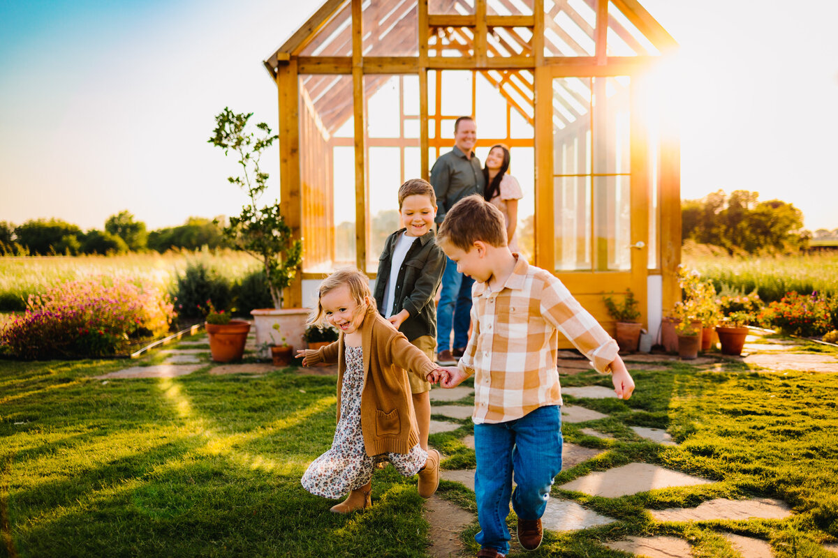 Family moment in spring for a mini session photography. Family members are playing in front of a small wooden house with glass windows.  All of them are smiling and having fun.