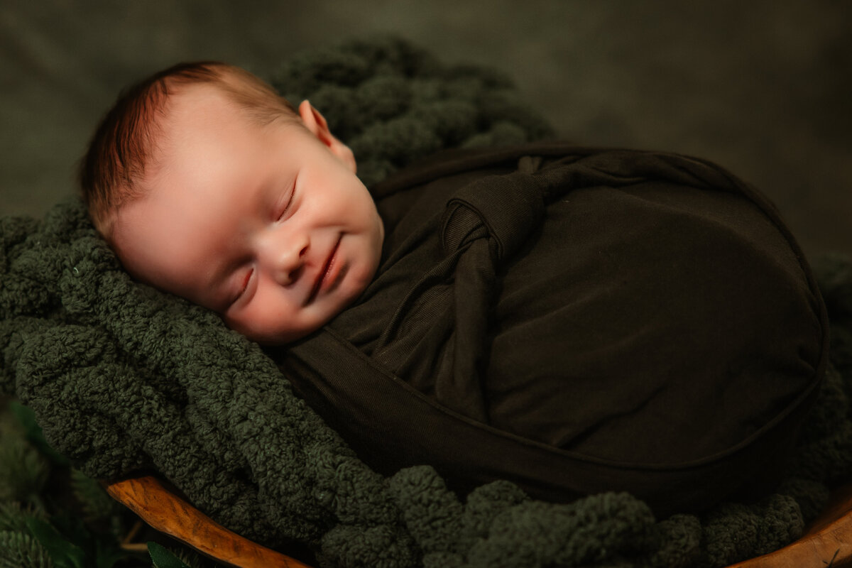 An image from a Milwaukee Newborn Photographer of a newborn baby smiling in its sleeps in a wooden bowl
