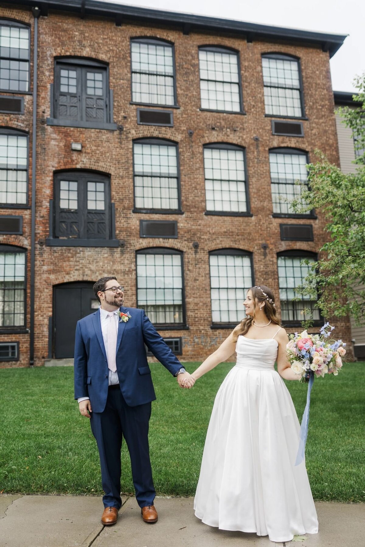 Bride and groom pose with The Roundhouse Hotel as their background, including the lawn and brick walls