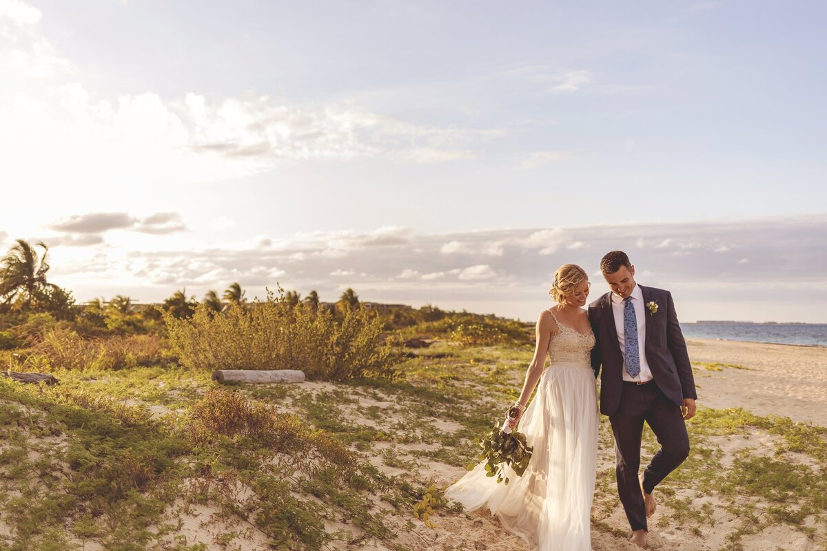 Bride and groom walking off beach dune at wedding in Cancun