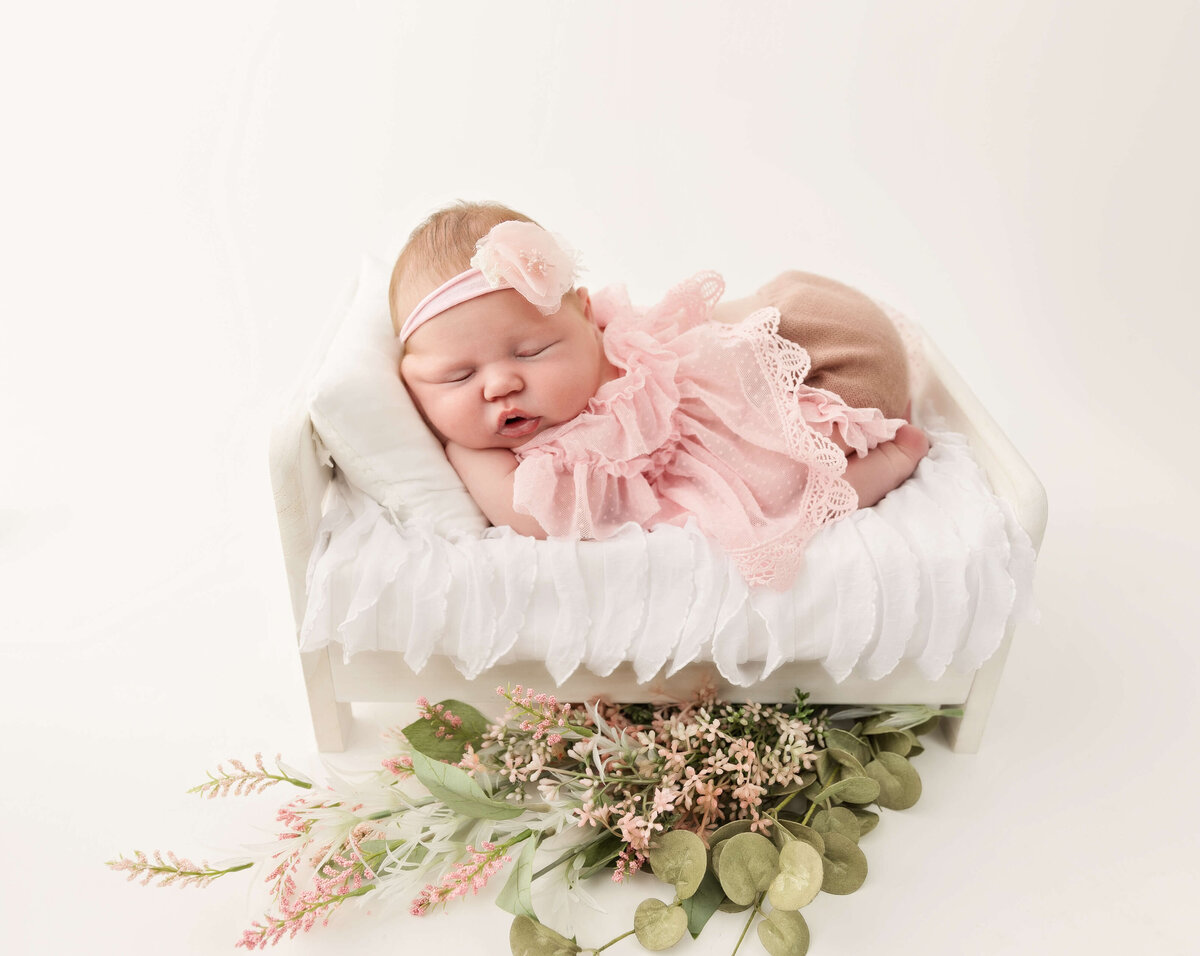 Newborn baby posed in a pink dress in a white bed in an Erie Pa photo studio