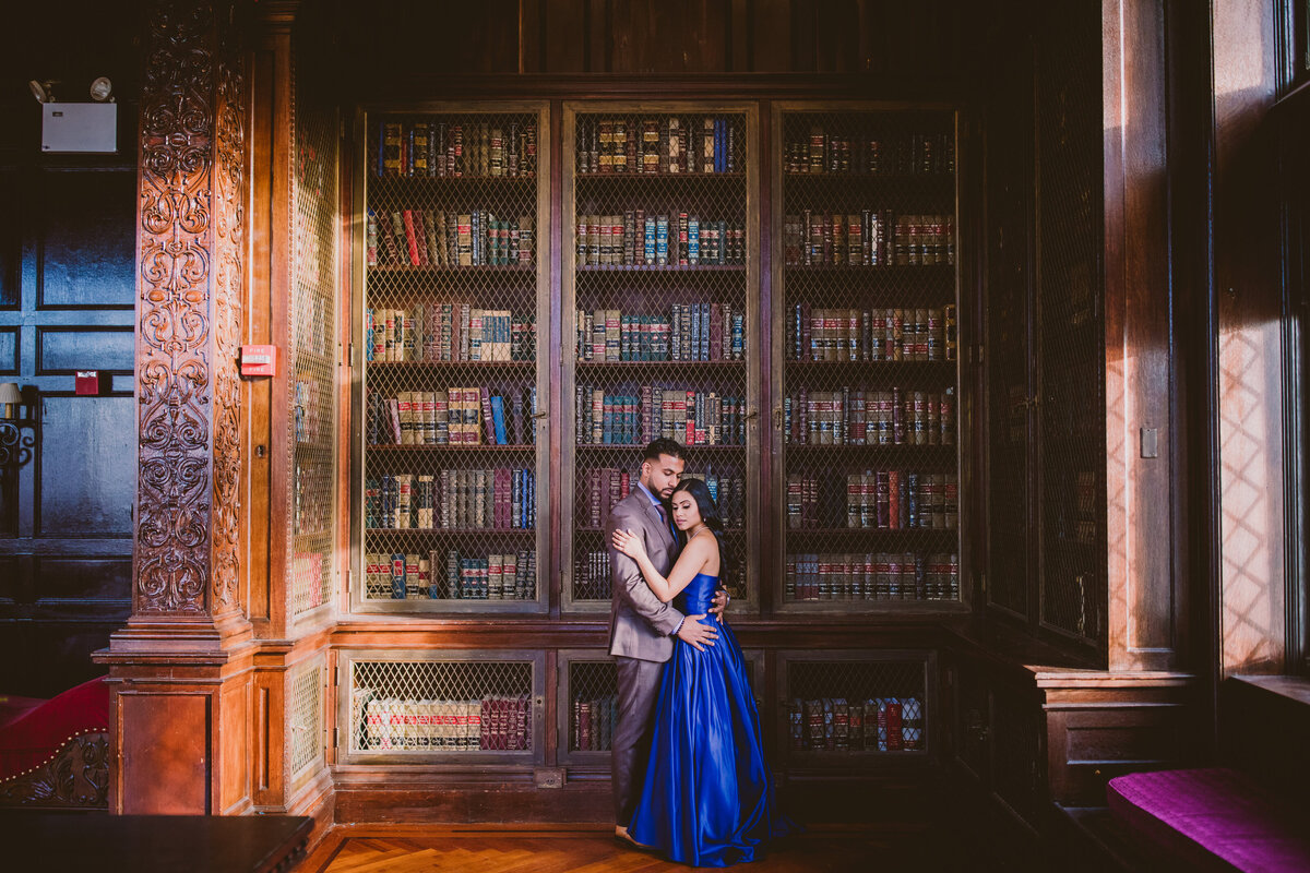 Engagement couple embracing in front of a bookshelf library at the hempstead house in sands point preserve in ny
