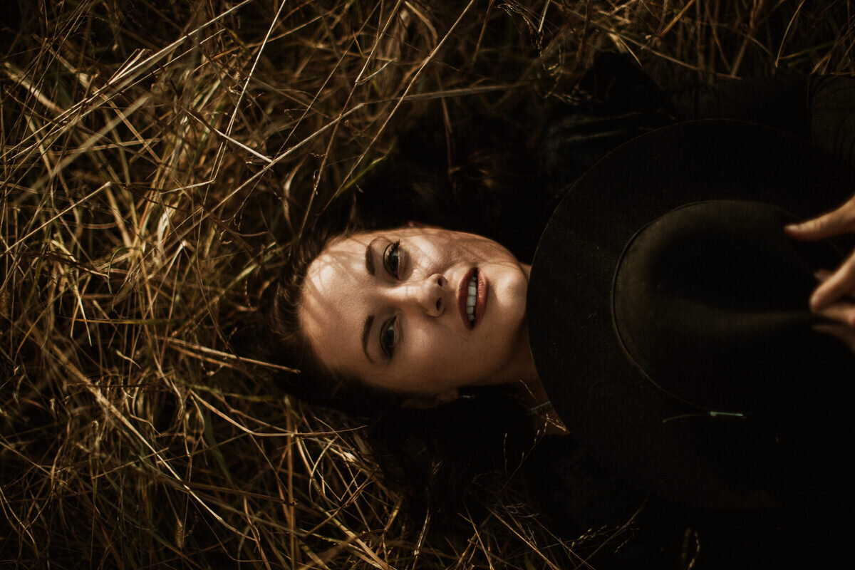 Woman laying in field holding hat looking into camera