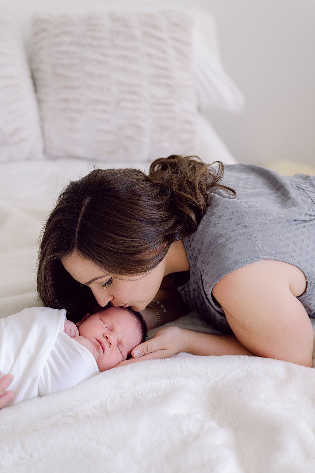 mom-kissing-newborn-baby-on-bed
