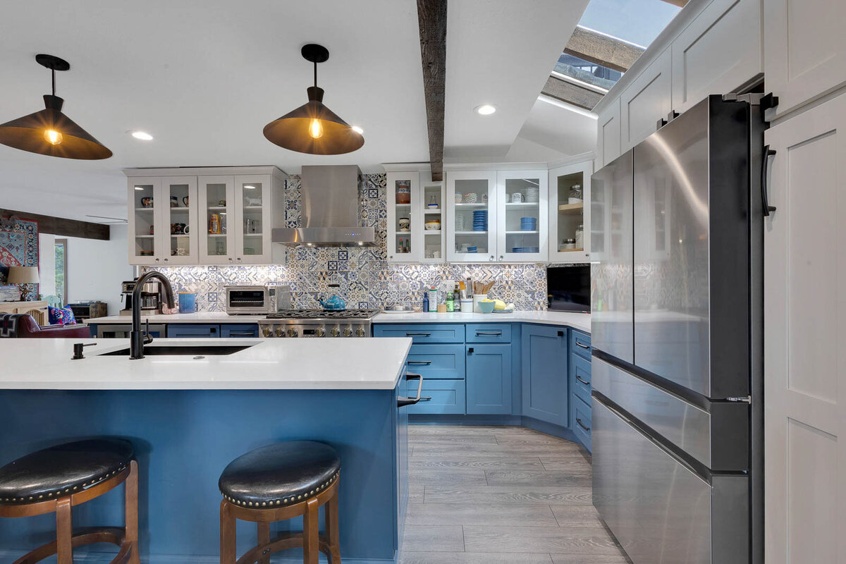 A blue themed kitchen with detailed back splash tiling and clear cabinet windows.