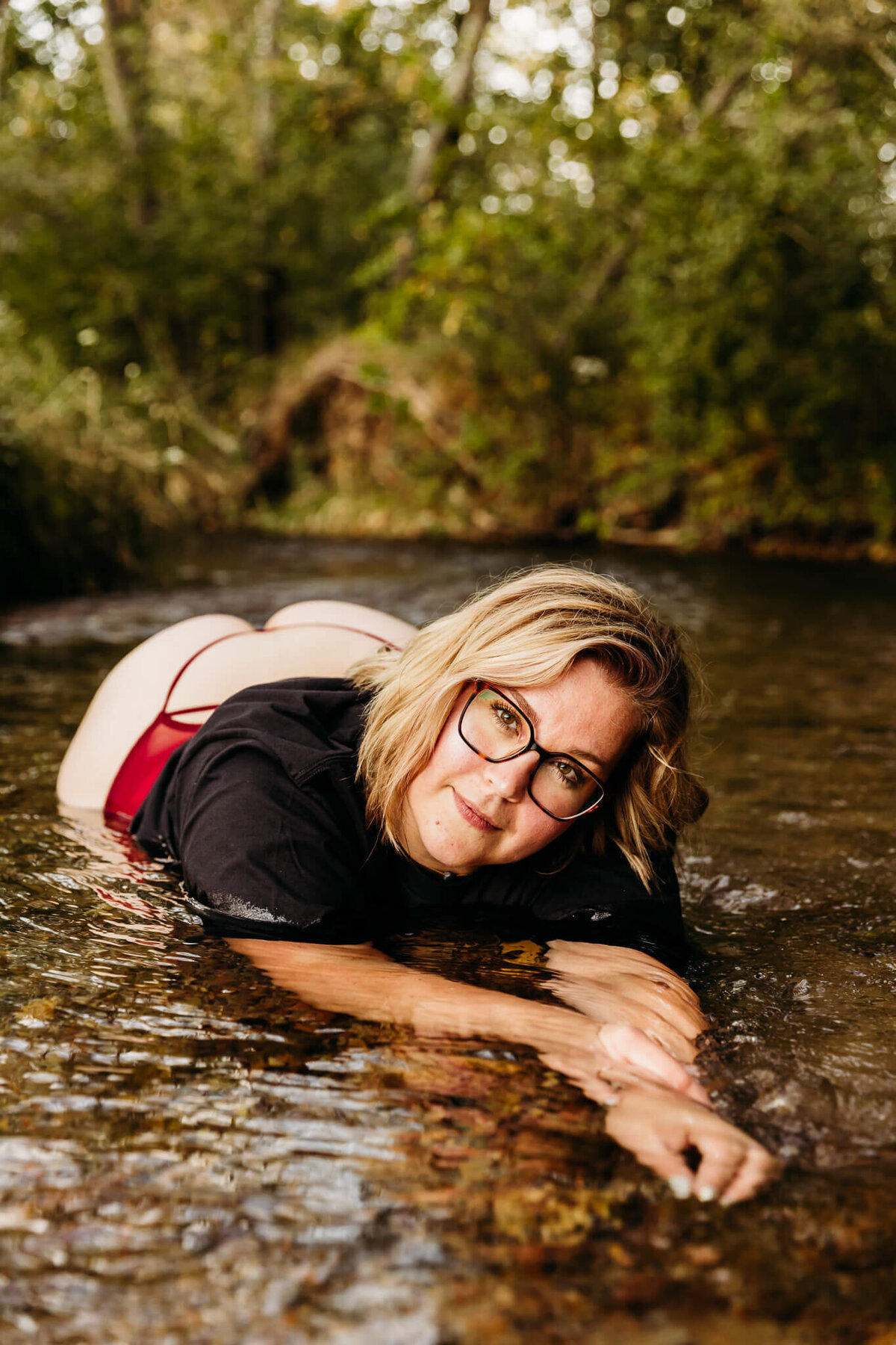 stunning woman in glasses laying in a creek in a tshirt and underwear