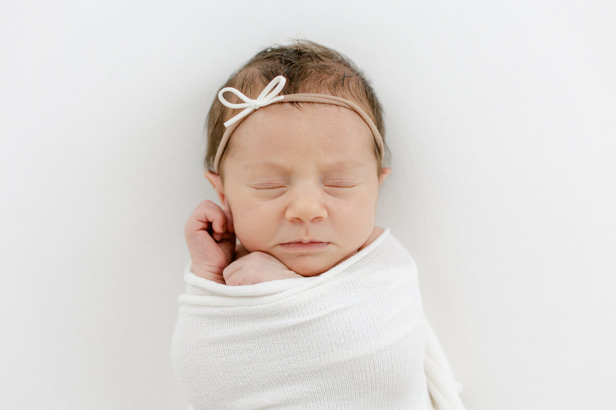 newborn baby girl swaddled with her hands close to her face while she sleeps for her newborn session photographed by Philadelphia Newborn Photographer Tara Federico