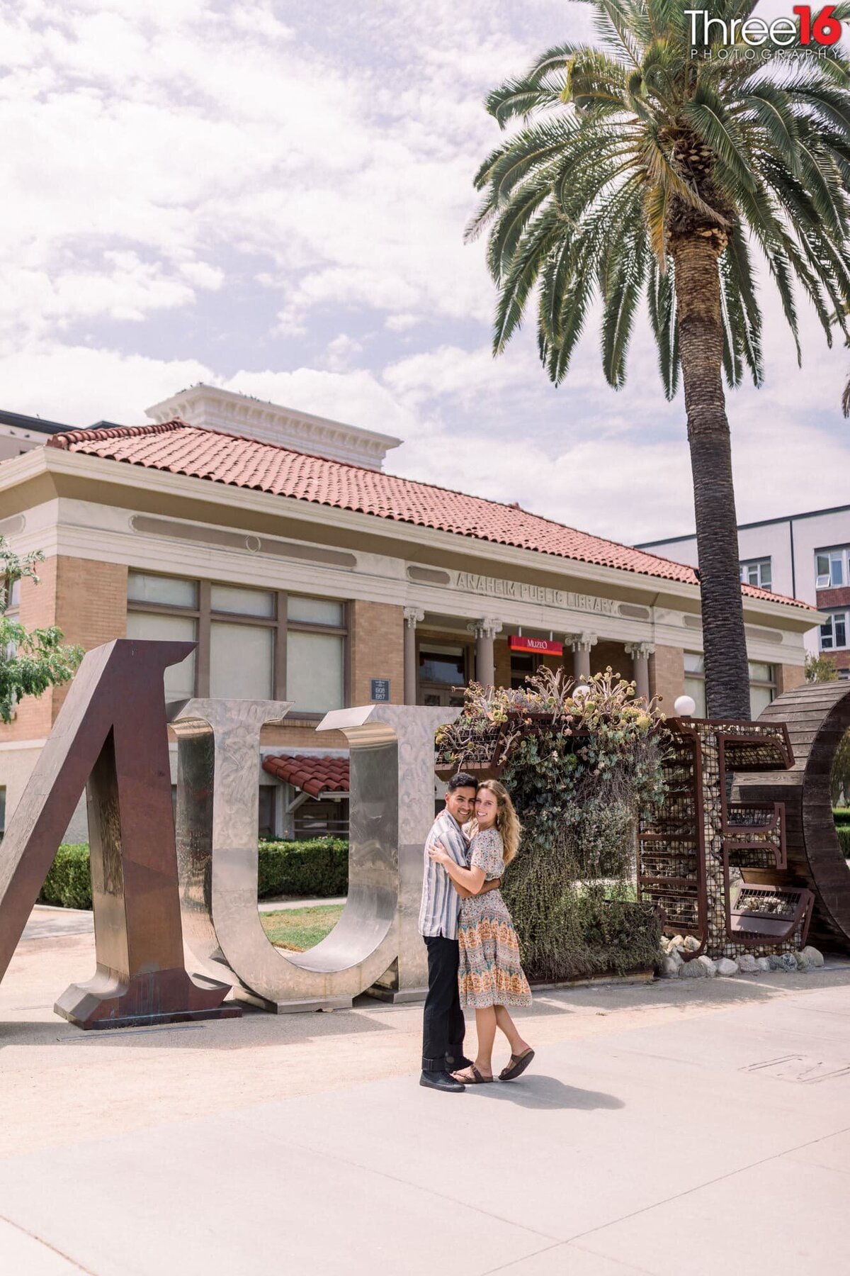 Soon to be married couple cozy up for a photo in front of the MUZEO sign out front of the Anaheim Public Library