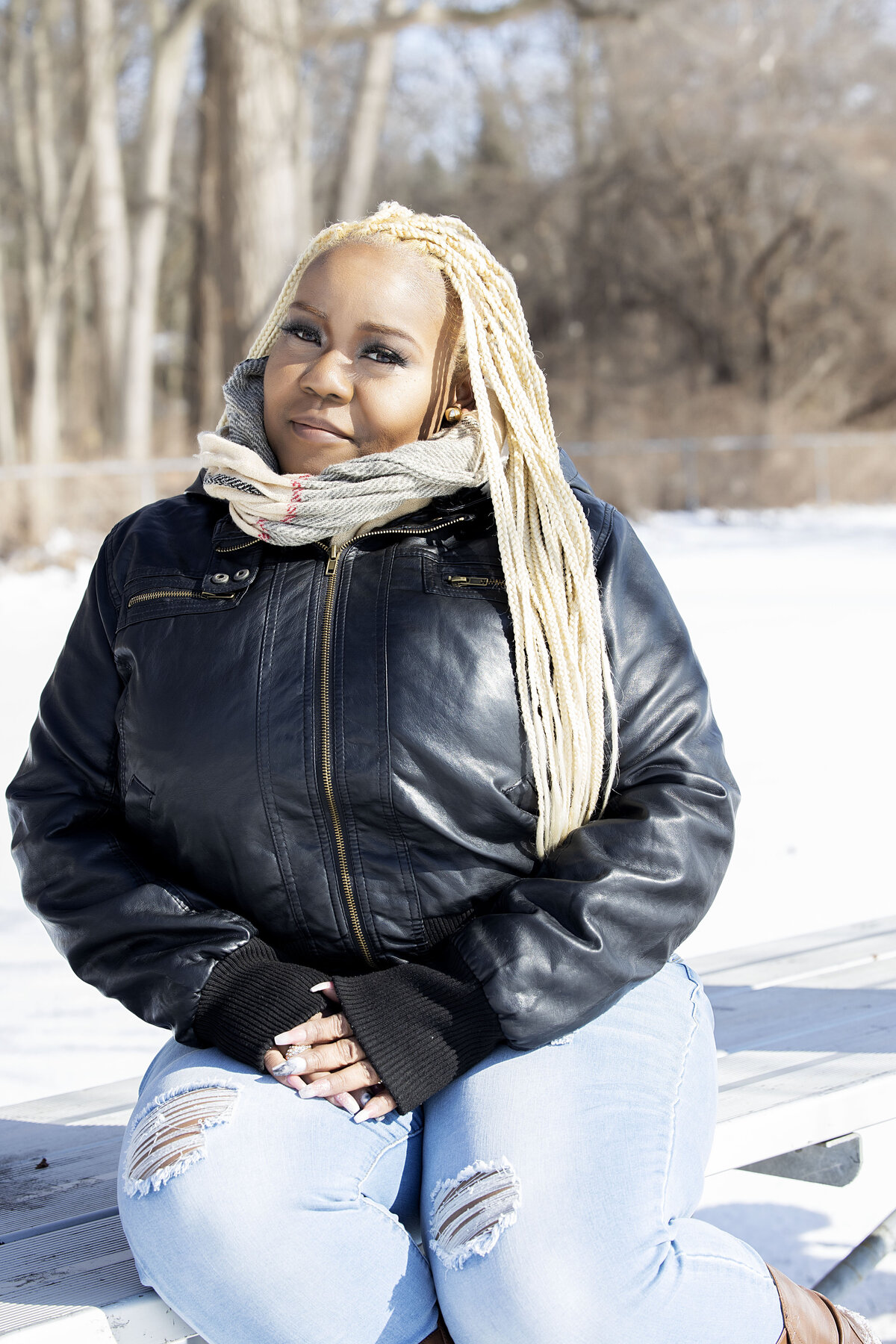 Woman in black leather jacket, blue jean top and jeans sitting on park bench