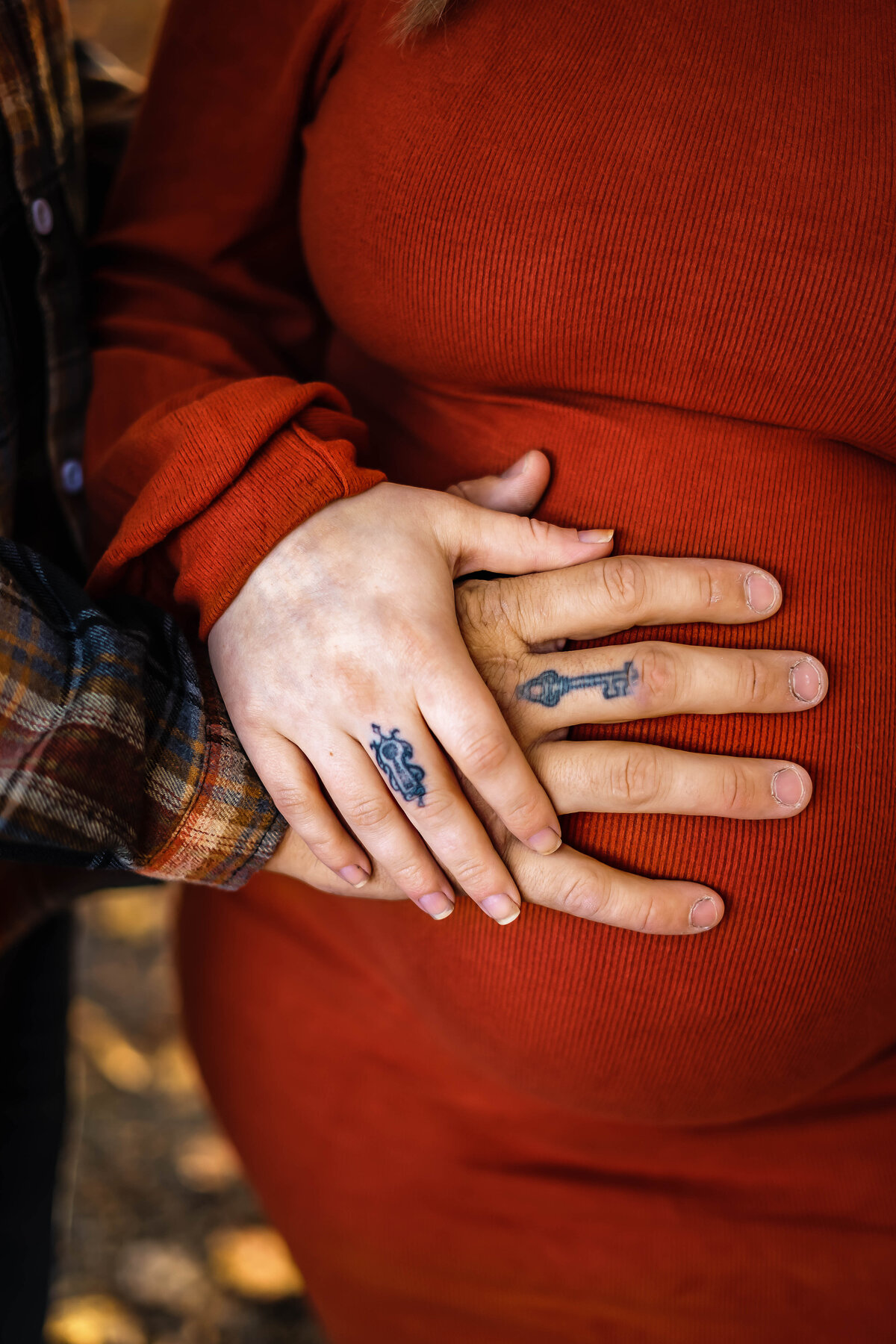 Couples hand on a pregnant belly wearing fall colors with key tattoos