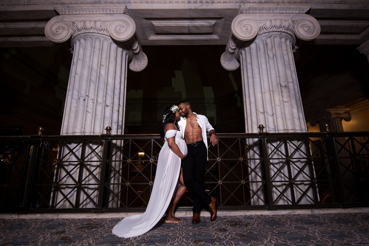 a couple kiss in front of two large columns for their maternity photography