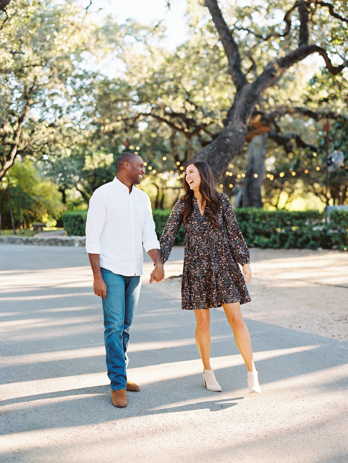 Man in white shirt and jeans and woman in a floral dress holding hands and smiling