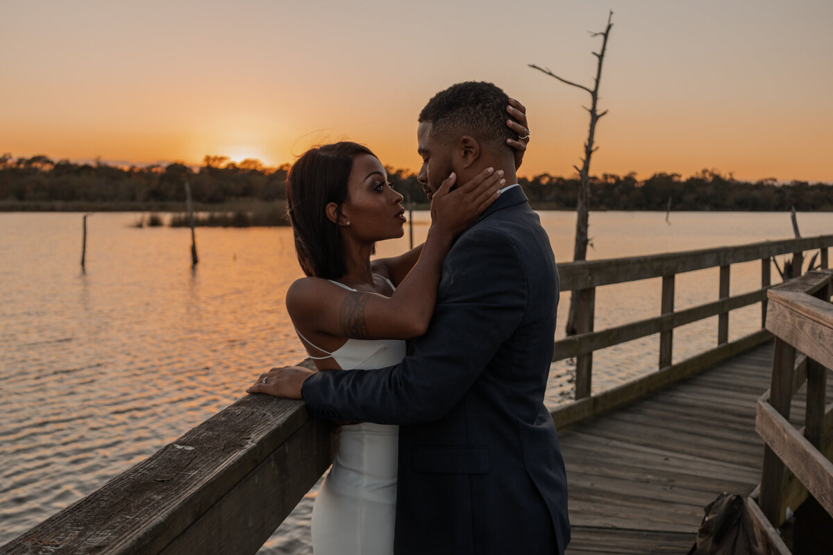 newly engaged black couple sharing an intimate moment during their engagement session at Bay Area Park in Houston, Texas. The couple embraces on a wooden pier overlooking a serene lake at sunset, capturing their love and connection.