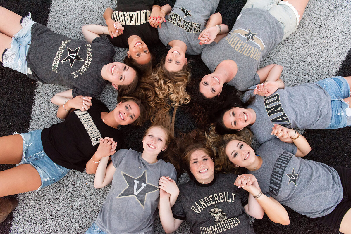Large group of Vanderbilt University seniors laying on the football field smiling up at the camera, they are wearing their school shirts and laughing together