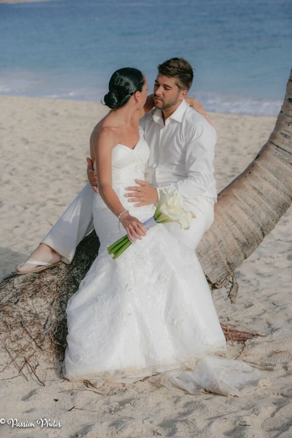 A couple relaxes on a palm tree trunk on a beach, enjoying a serene moment together. This image captures the relaxed and romantic atmosphere of destination weddings, showcasing the natural beauty and unique settings that make each wedding unforgettable.