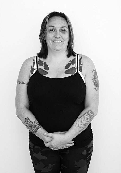 Black and white before shot of a tattooed woman in a tank top, standing confidently against a white backdrop.