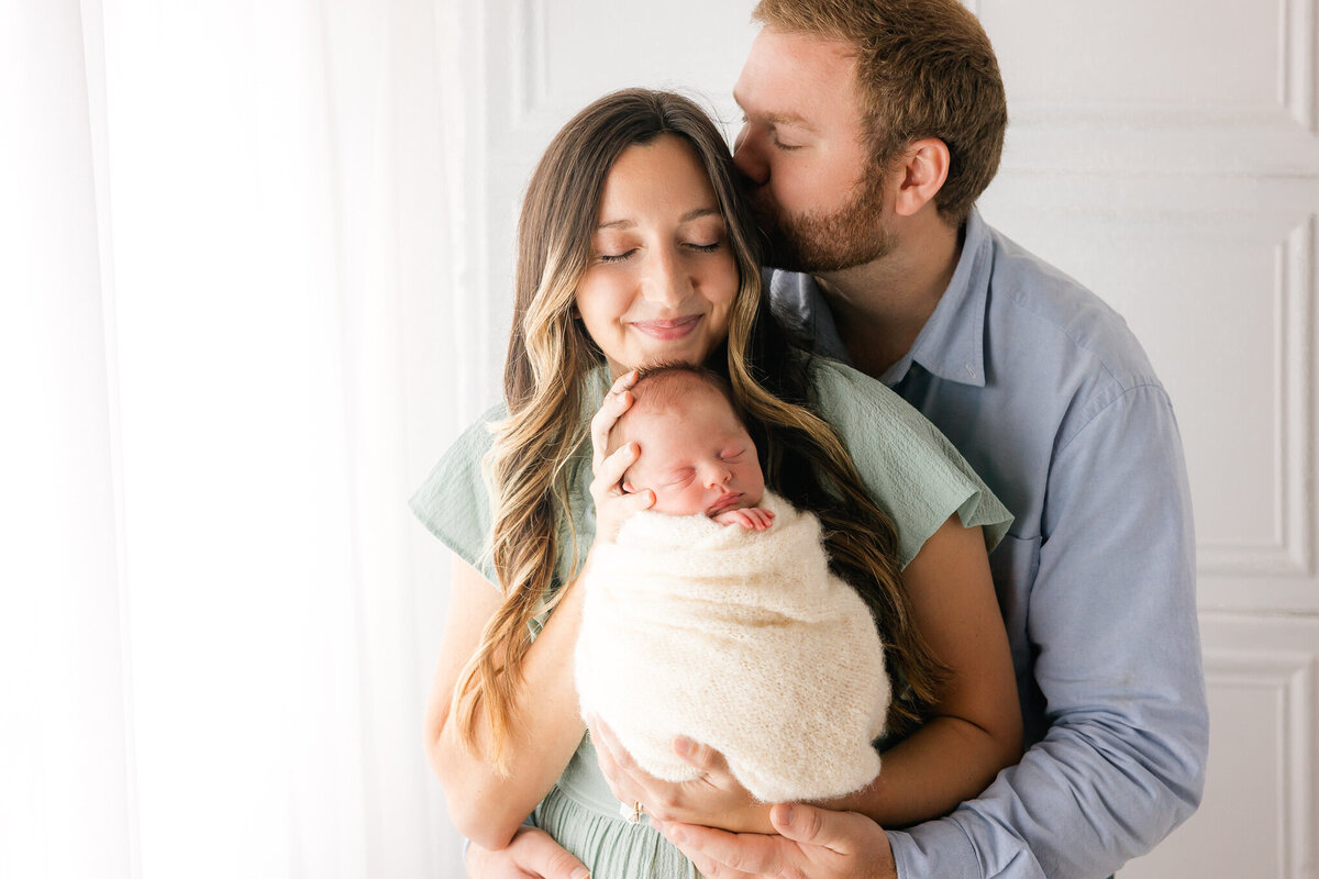 Young mom and dad holding their baby boy who is wrapped in a cream wrap with Constance Calton Photography
