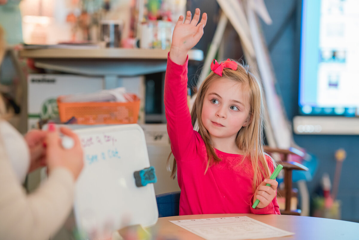 Young girl sitting with her hand raised in her classroom