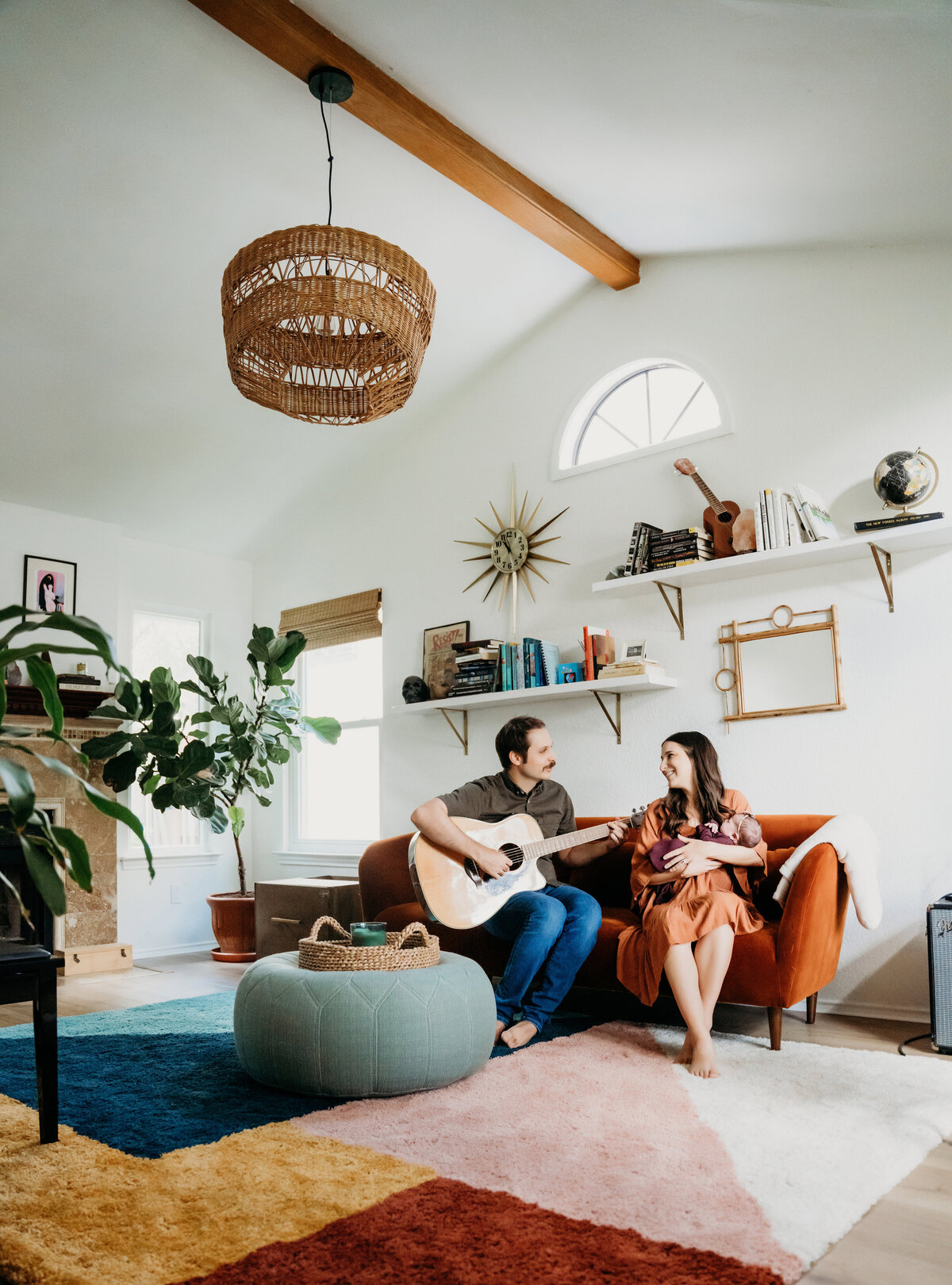 Newborn Photographer, a father plays the guitar as mom holds baby beside him in the living room
